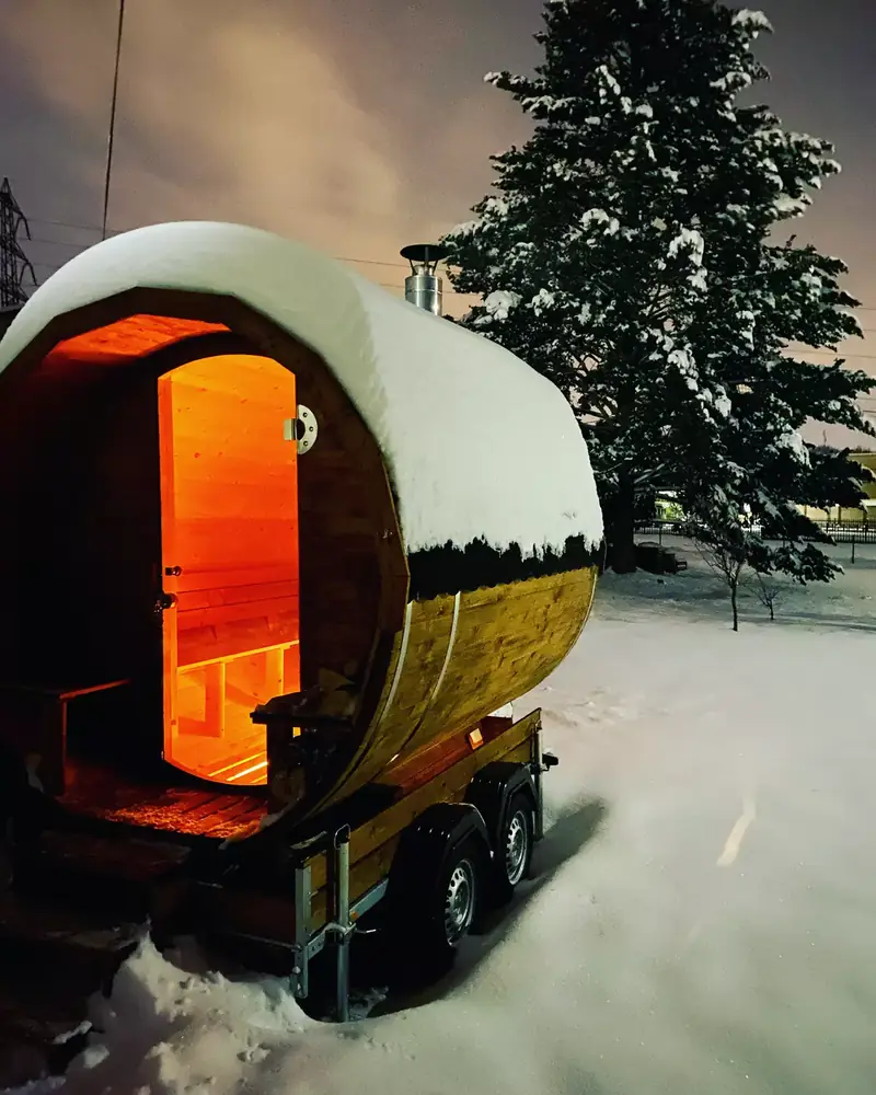Mobilní sauna v zimě pod sněhem, uvnitř svítí kamna
